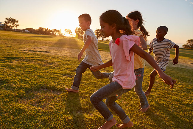 Children running barefoot through a grassy field at sunset