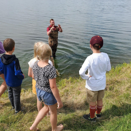 Four students watch as a teacher collects freshwater sponges from a lake