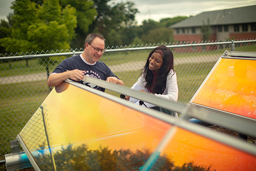 A black student examines a translucent orange solar panel along with her teacher