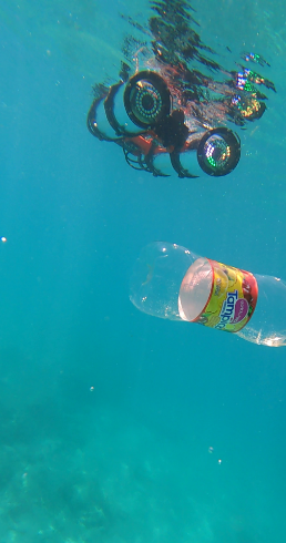 An underwater picture of a robot swimming p to a plastic water bottle