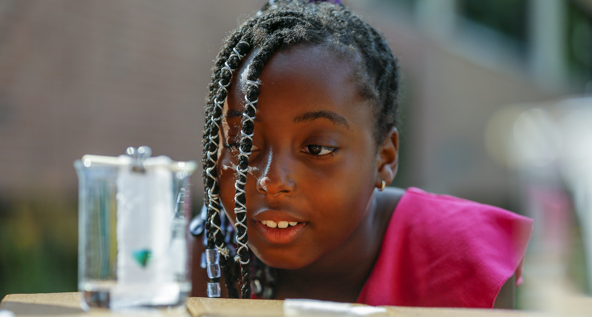 A child examines a science experiment closely in a jar on the table