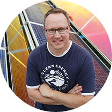 A picture of Troy Goodnough standing arms crossed in front of colorful solar panels
