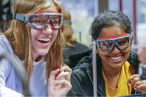 Two students wearing lab goggles and smiling